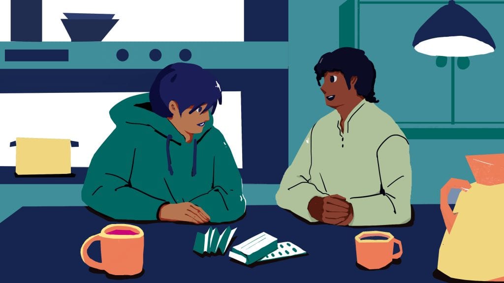 A young person and an adult having a conversation at a kitchen table, with cups and a box of medication, in a modern kitchen setting.