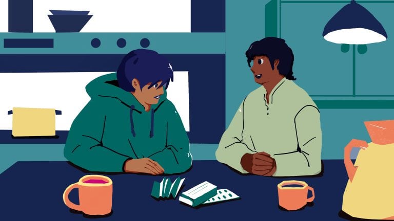 A young person and an adult having a conversation at a kitchen table, with cups and a box of medication, in a modern kitchen setting.
