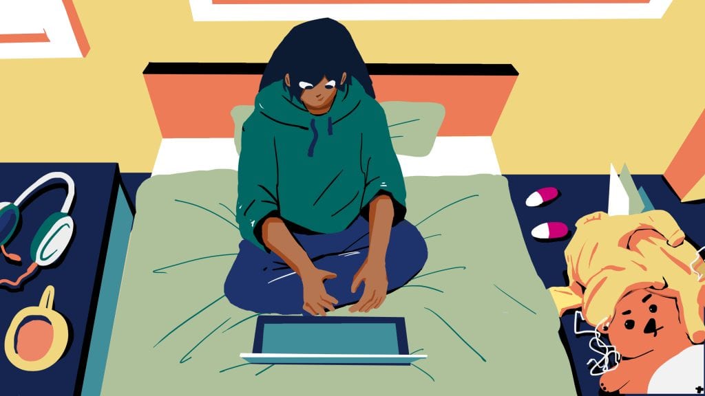 A woman sitting cross-legged on a bed, using a laptop with headphones nearby, in a cozy bedroom setting.