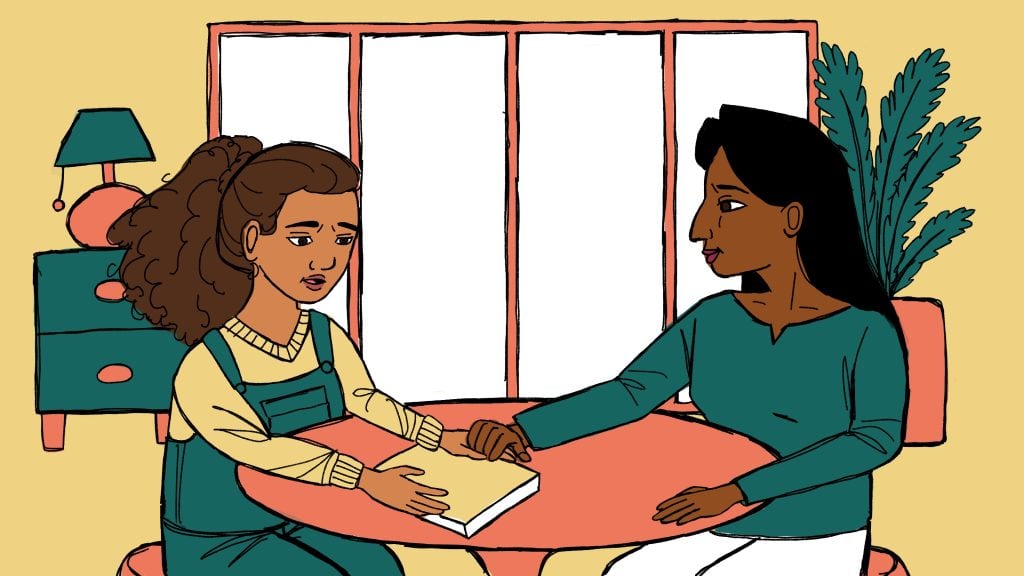 A woman comforting a young girl who appears upset, sitting together at a table in a cozy room with a large window and houseplant in the background.