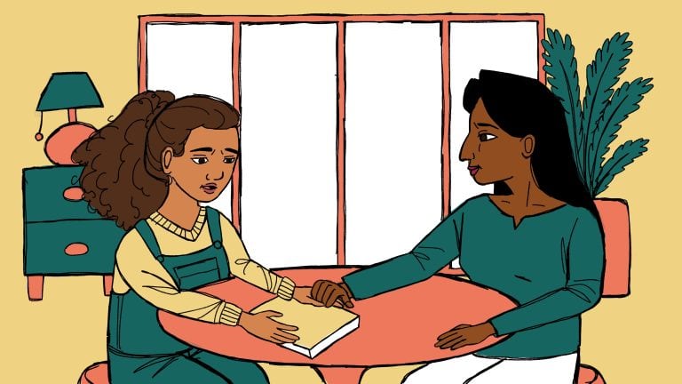 A woman comforting a young girl who appears upset, sitting together at a table in a cozy room with a large window and houseplant in the background.