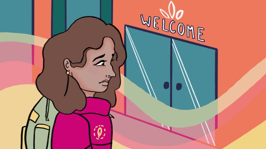 A woman with brown hair and a pink scarf standing outside a building with a "Welcome" sign above the door.