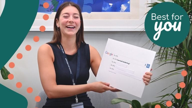 A woman smiling and holding a large Google search box sign at an indoor event, promoting digital literacy and online search skills.